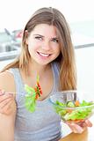 Smilling woman eating salad in the kitchen