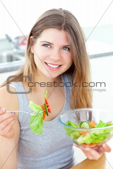 Smilling woman eating salad in the kitchen