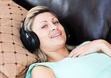 Smiling woman lies on a sofa and listen music
