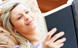 Radiant woman lies on sofa and reading a book 