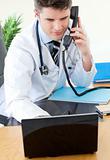 Positive male doctor on phone using his laptop