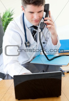 Positive male doctor on phone using his laptop