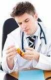 Serious male doctor holding pills sitting at his desk 