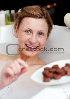 Happy woman eating chocolate while having a bath