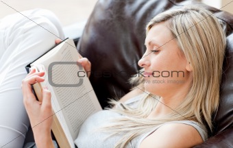 Charming woman reading a book sitting on a sofa 