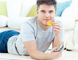 Relaxed young man eating crisps holding a remote