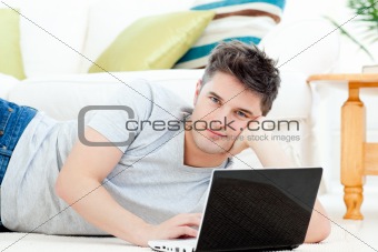 Handsome young man lying on the floor with a laptop