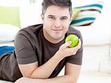 Positive man holding a green apple lying on the floor