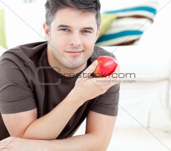 Jolly man holding a red apple lying on the floor 