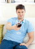 Charming young man sitting on a sofa holding wineglass