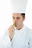 Young cook with closed eyes tasting a herb against white backgro