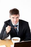 Charming businessman using a laptop while having breakfast