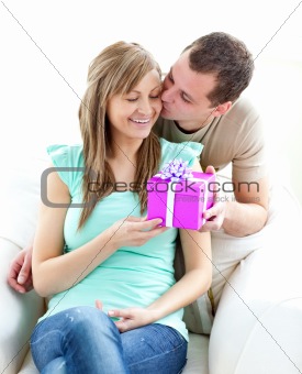 Attractive boyfriend giving a present and a kiss to his glowing 