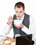 Concentrated businessman eating cereals looking at his laptop 