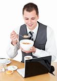Happy businessman eating cereals looking at his laptop 