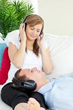 Cute woman listening to music with her boyfriend lying on a sofa