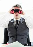 Impressed businessman looking through binoculars sitting in his 