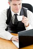 Happy young businessman looking at his laptop holding a coffee