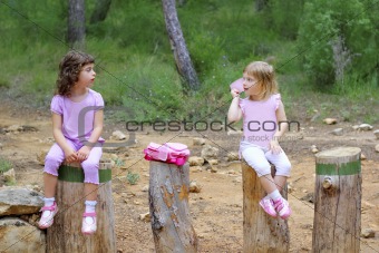two little girls sit on forest park tree trunks