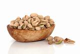 Pistachio nuts in an olive wood bowl and scattered, isolated over white background with reflection. Pistacia vera.