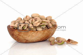 Pistachio nuts in an olive wood bowl and scattered, isolated over white background with reflection. Pistacia vera.