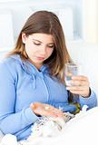 Sick woman taking pills holding a glass of water sitting