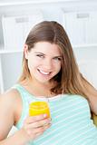 Charming young woman holding a glass of orange juice sitting on a sofa