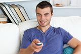 Smiling young man holding a remote sitting on a sofa