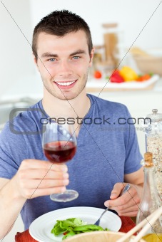 Cute man eating a healthy salad with some wine 