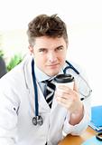 Serious male doctor drinking coffee in the office