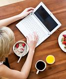 Close-up of a caucasian woman using a laptop drinking coffee eating muesli