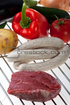 raw meat, sausages and vegetables on a gridiron