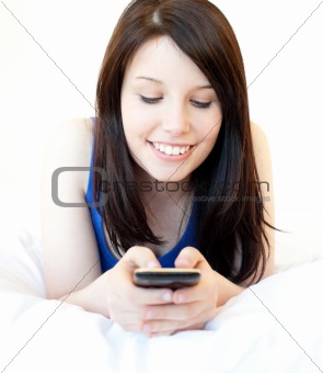 Happy female teenager using cellphone lying on the bed 