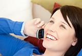 Cheerful female teenager talking on phone lying on a sofa