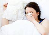 Sick young woman using a tissue lying in a bed