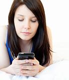Concentrated young woman texting while lying on a bed against white background