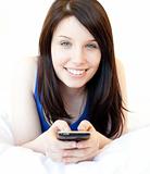 Happy young woman texting while lying on a bed 