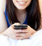Close-up of a brunette teenager texting while lying on her bed 