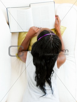 Young afro-american woman reading a book lying on the couch 
