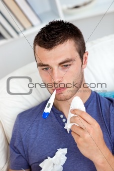 Morbid caucasian man sitting on the sofa with thermometer and ti