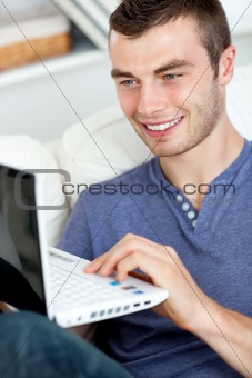 Joyful young man sitting on the sofa using his laptop 
