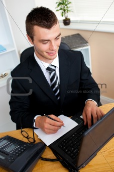 Delighted businessman looking at his laptop and writing