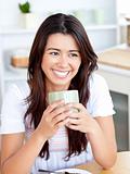 Beautiful asian woman holding a cup sitting in the kitchen 