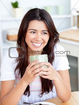 Beautiful asian woman holding a cup sitting in the kitchen 