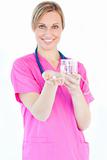 Bright female nurse holding pills and a glass water smiling at t