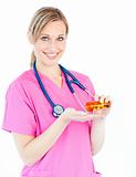 Confident female nurse holding pills smiling at the camera 
