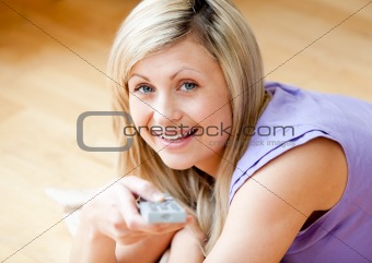 Glowing blond woman watching TV holding a remot lying on the floor