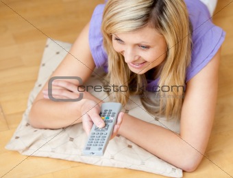 Glowing woman watching TV holding a remote lying on the floor