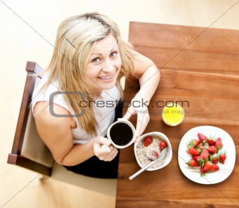 Close-up of a woman using a laptop holding a cup of coffee eating muesli