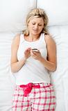 Bright woman sending a text lying on a bed at home